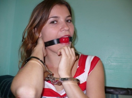 Clothed girl cuffs herself at wrists and ankles before affixing a ball gag 89633259