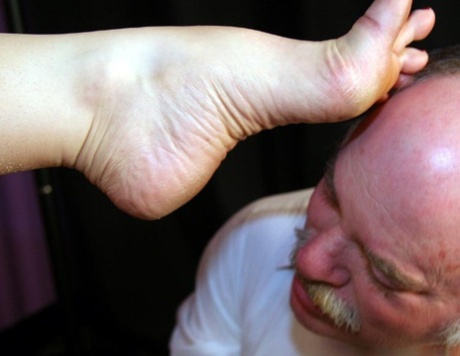 Redheaded woman rubs her bare feet over an older man's face 23210089